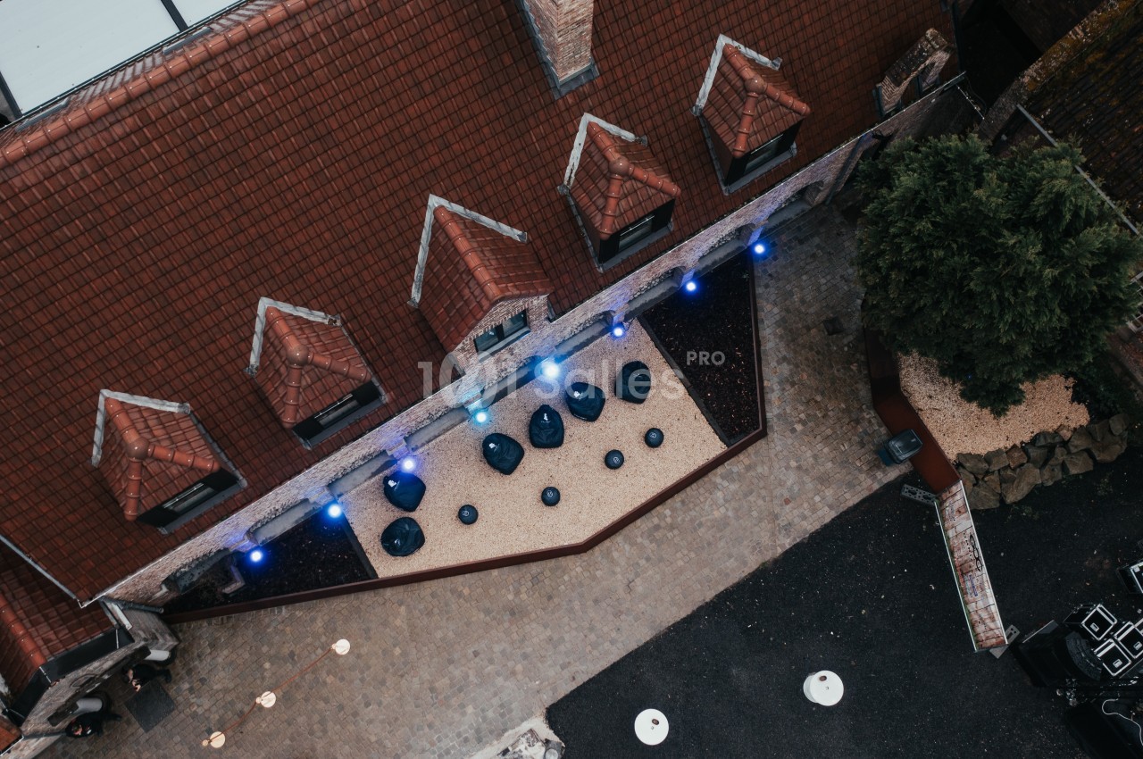 Vue aérienne d'une cour pavée avec des toits en tuiles, des tables rondes et des lumières bleues installées.