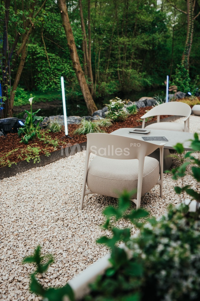 Deux chaises et une table sur un sol en gravier dans un jardin verdoyant avec des plantes et un éclairage discret.