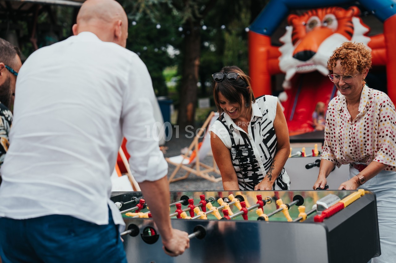 Des adultes jouent au baby-foot en extérieur, avec une structure gonflable en forme de tigre en arrière-plan.