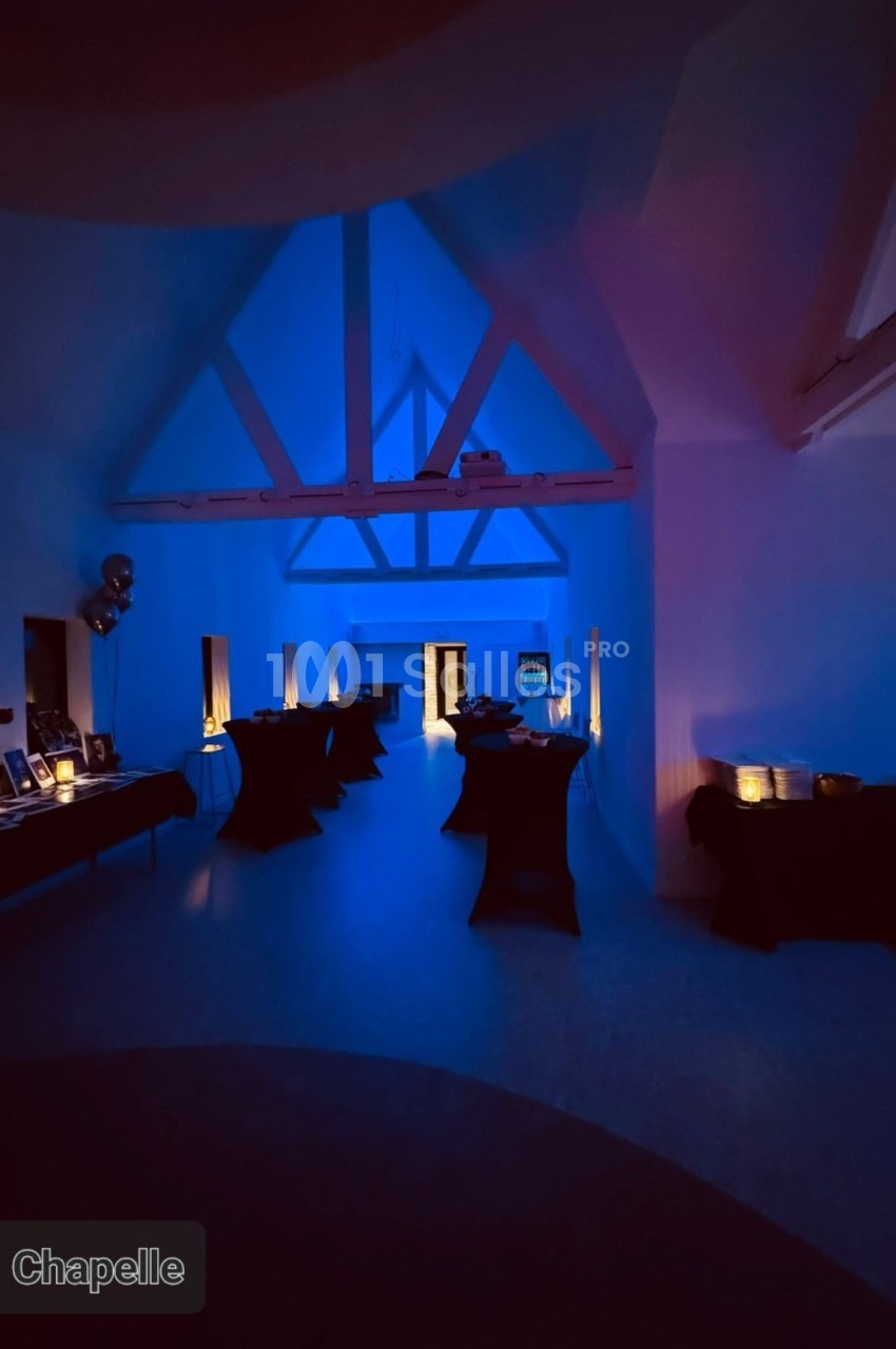 Salle éclairée par une lumière bleue tamisée, avec des tables noires dressées le long des murs.