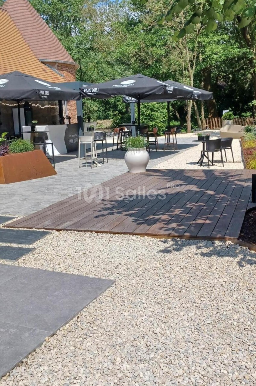 Terrasse extérieure avec tables, chaises, parasols noirs et végétation environnante sous un ciel dégagé.