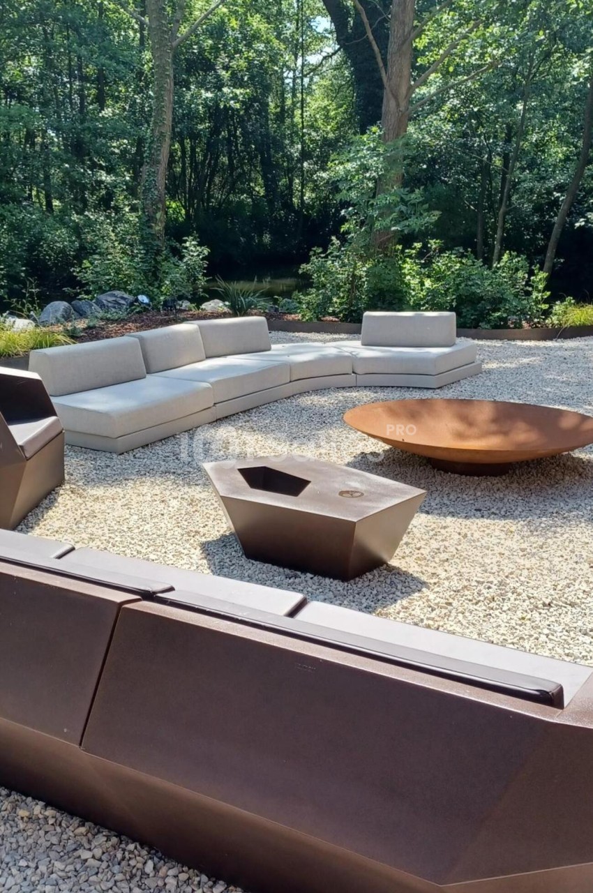 Salon de jardin moderne avec canapés et table basse sur une terrasse en gravier, entourée de végétation dense.