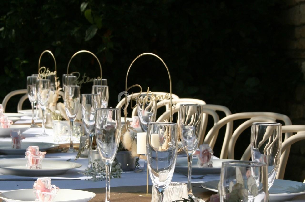 Table décorée pour un événement, avec verres, assiettes, fleurs et ornements dorés, en extérieur sous une lumière naturelle.