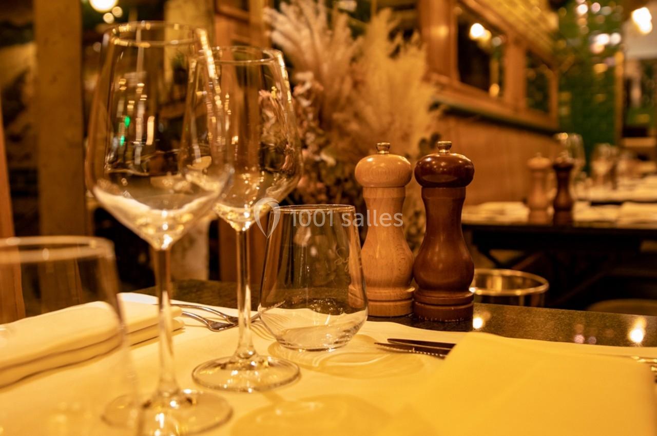 Table dressée avec verres à pied, moulin à sel et poivre, dans un restaurant à l'éclairage chaleureux.