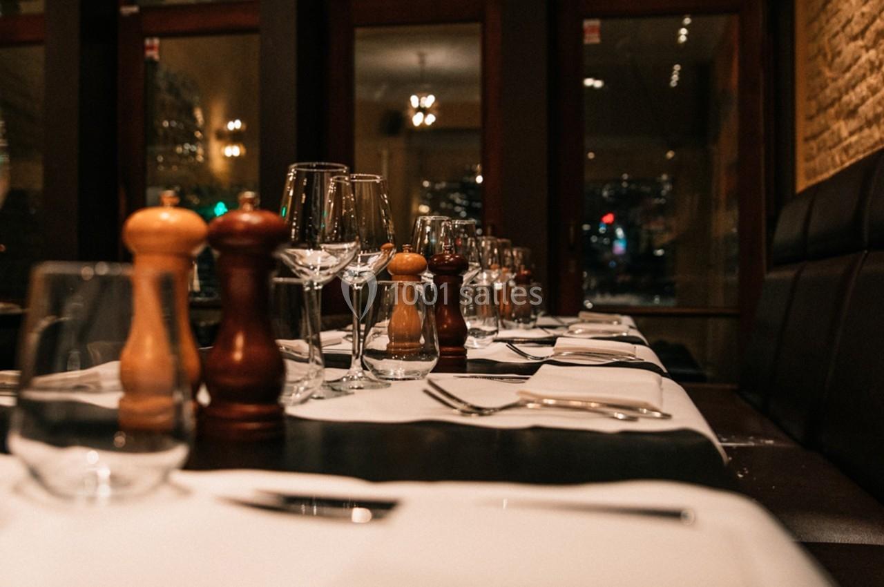 Table dressée dans un restaurant élégant avec nappes blanches, verres, couverts et moulins à épices alignés.