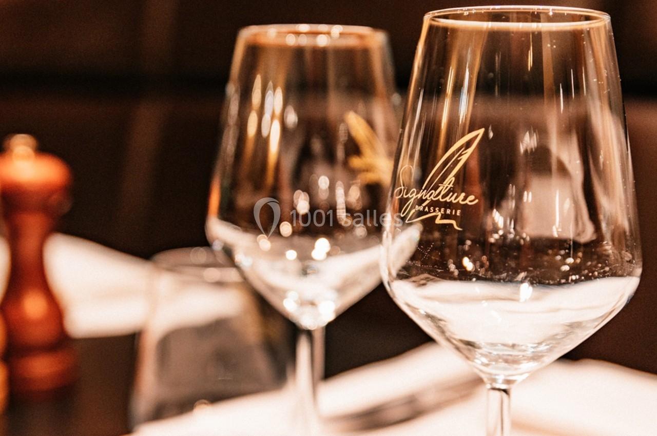 Deux verres à vin gravés posés sur une table de restaurant, avec un moulin à poivre flou en arrière-plan.