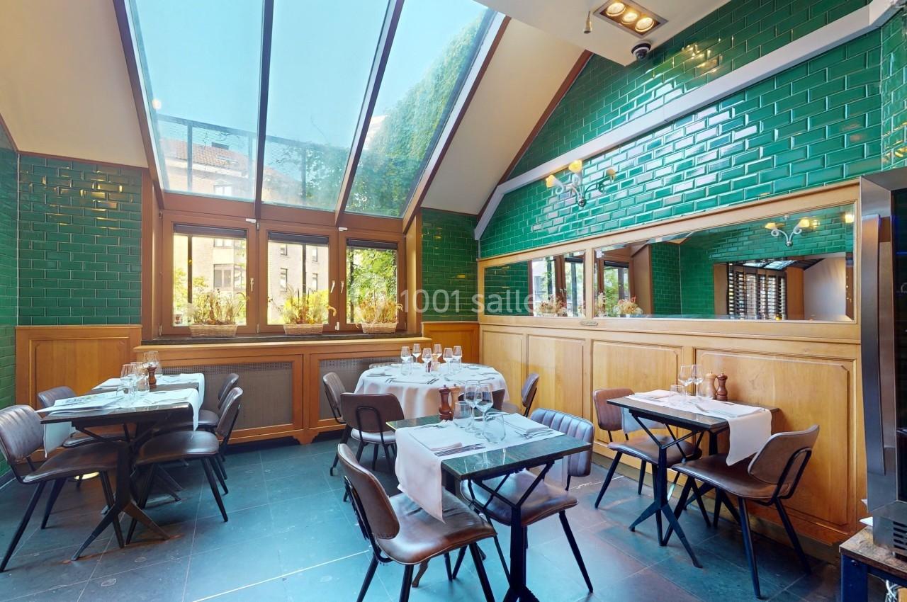 Salle de restaurant lumineuse avec tables dressées, murs en carreaux verts et grandes fenêtres donnant sur l'extérieur.