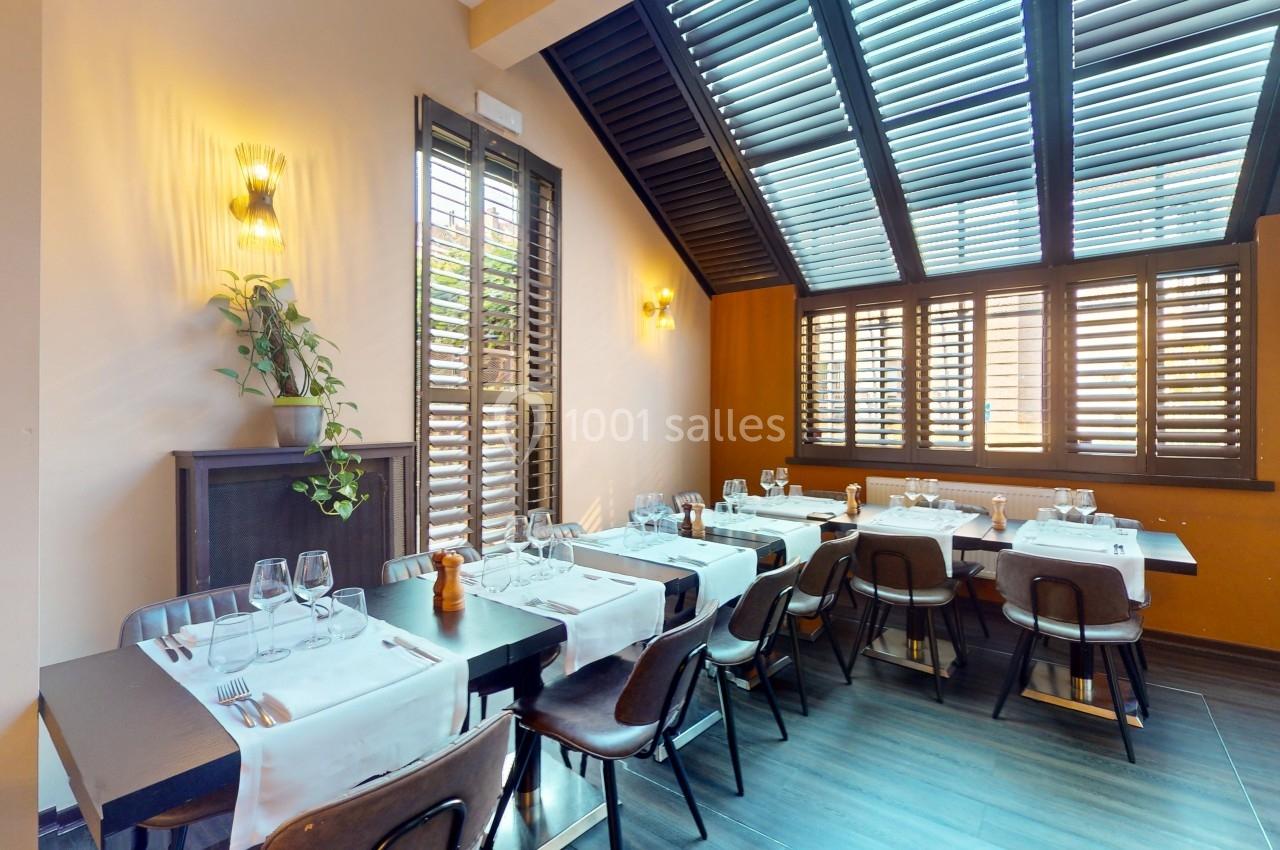 Salle de restaurant lumineuse avec tables dressées, chaises en bois et grandes fenêtres à persiennes.