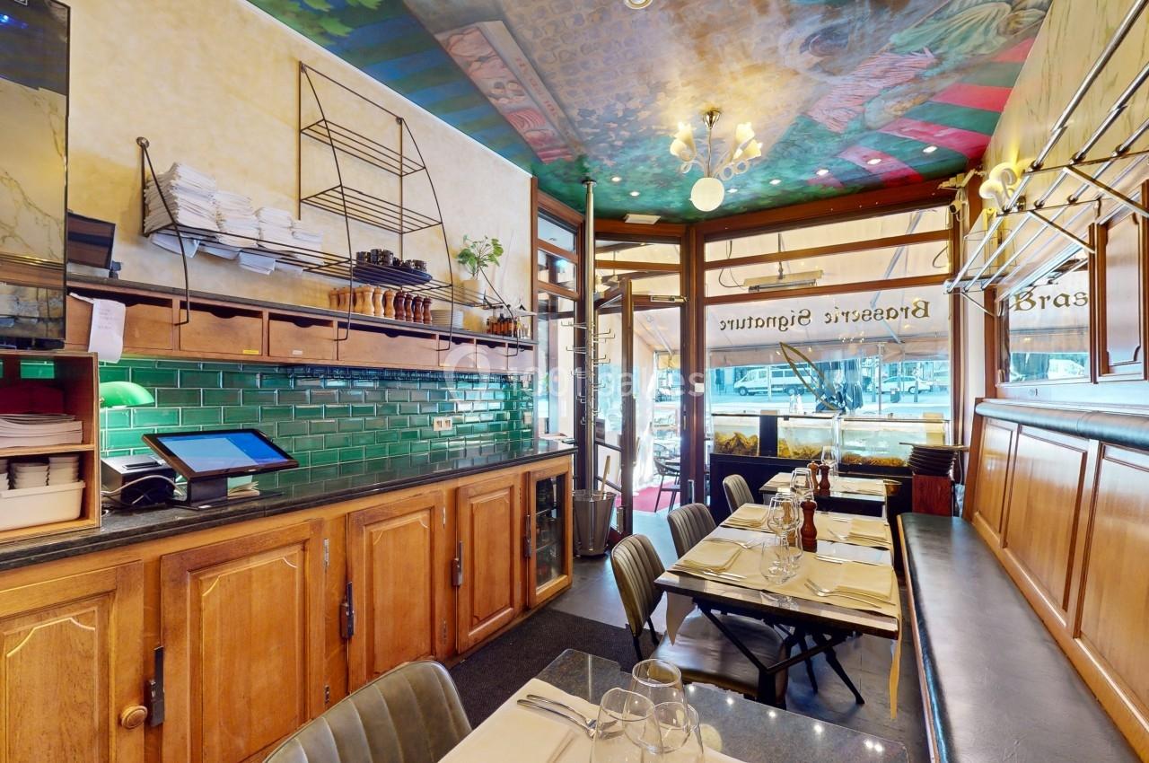 Intérieur d'un restaurant avec comptoir en bois, carrelage vert, tables dressées et plafond décoré.