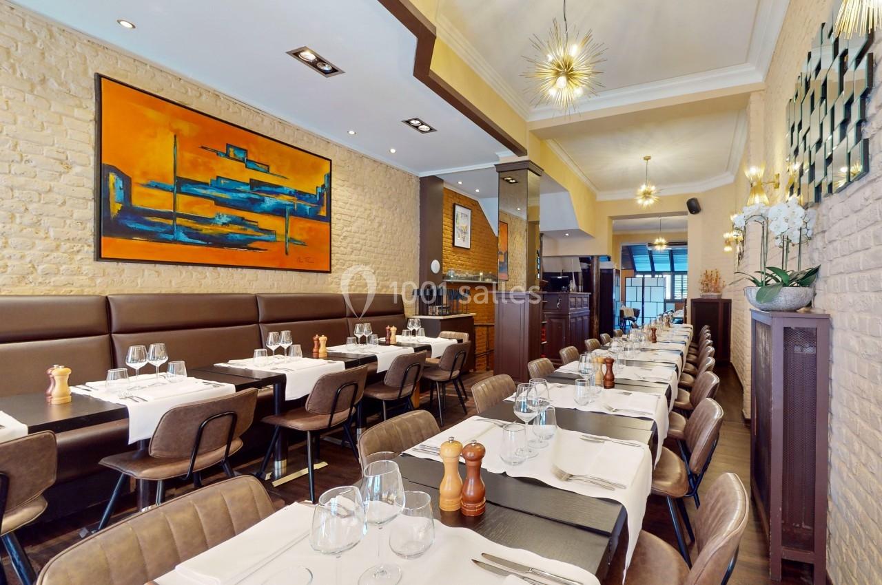 Salle de restaurant élégante avec tables dressées, murs en briques, tableau coloré et éclairage moderne.