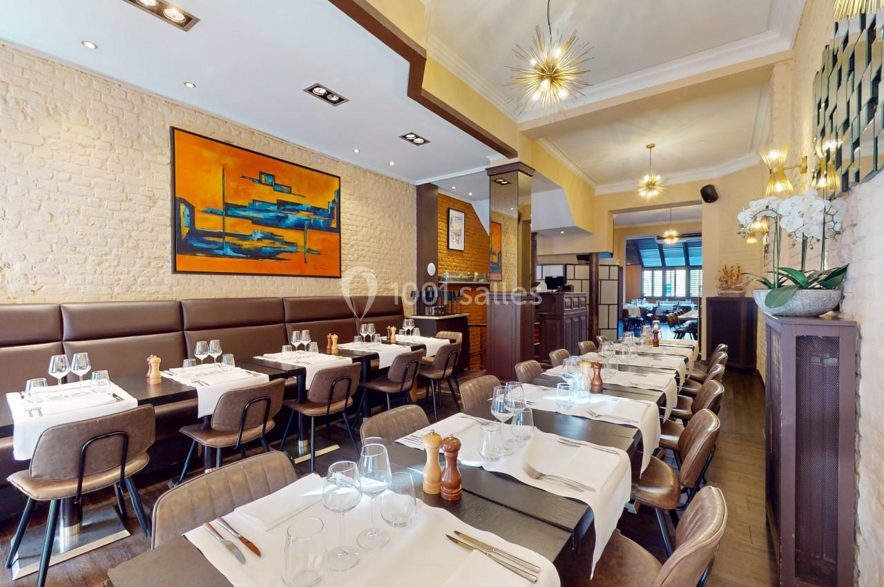 Salle de restaurant lumineuse avec tables dressées, murs en briques, tableau coloré et décoration moderne.
