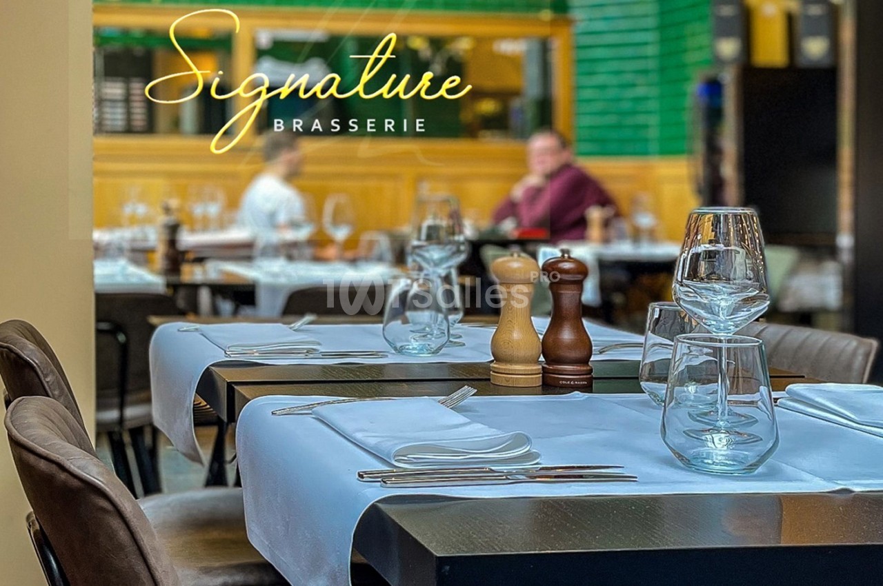 Table de restaurant élégamment dressée avec verres, couverts et moulins à épices, ambiance conviviale en arrière-plan.