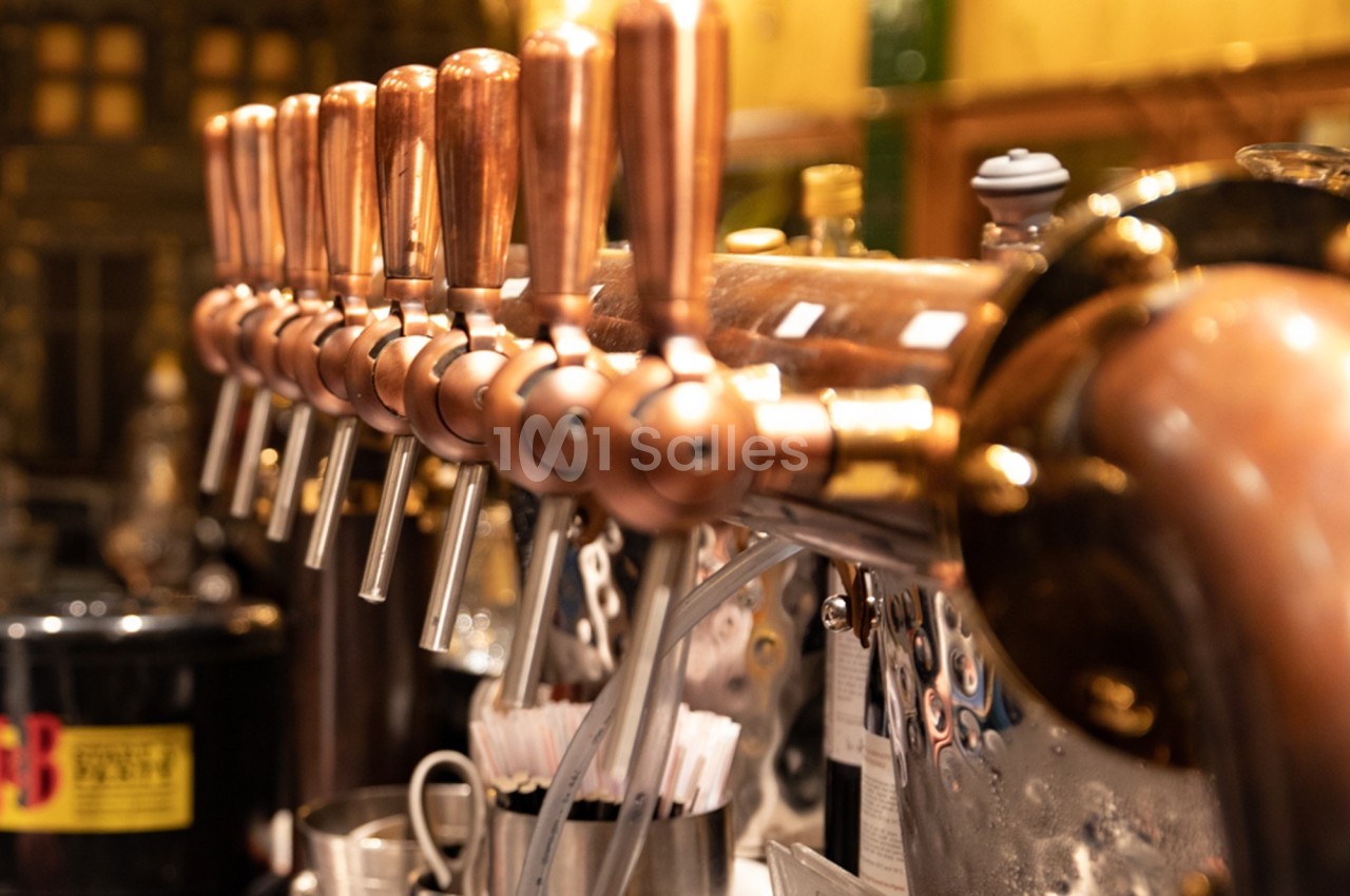 Robinetterie en cuivre alignée sur un comptoir, utilisée pour le service de boissons dans un bar ou une brasserie.