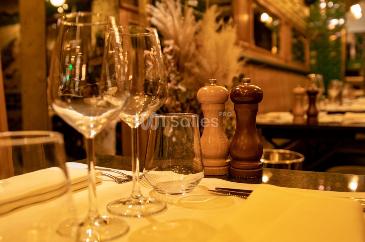 Table dressée avec des verres, couverts et serviettes, décorée de moulins à poivre dans un restaurant chaleureux.