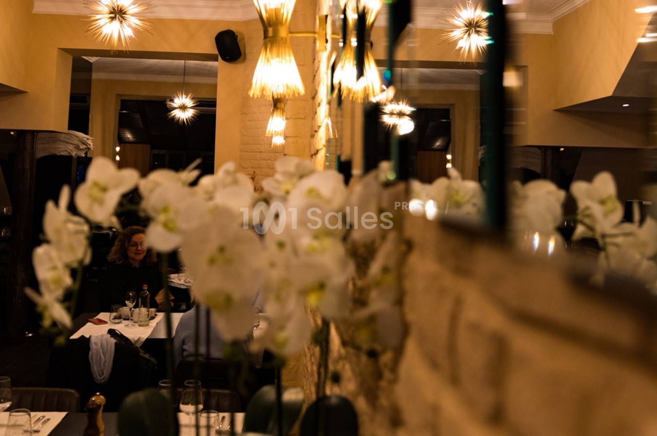 Salle de restaurant chaleureuse avec éclairage tamisé, murs en pierre et orchidées blanches au premier plan.
