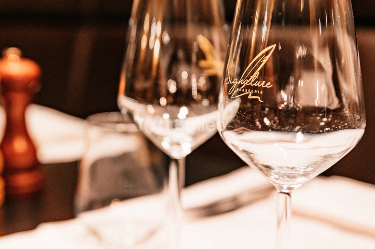 Deux verres à vin transparents posés sur une table dressée avec un moulin à poivre en arrière-plan flou.