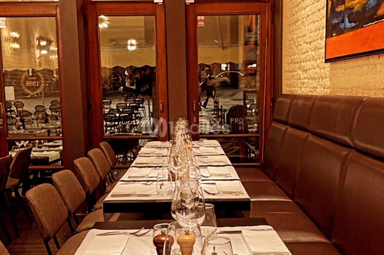 Salle de restaurant avec tables dressées, chaises alignées et grandes baies vitrées donnant sur l'extérieur.