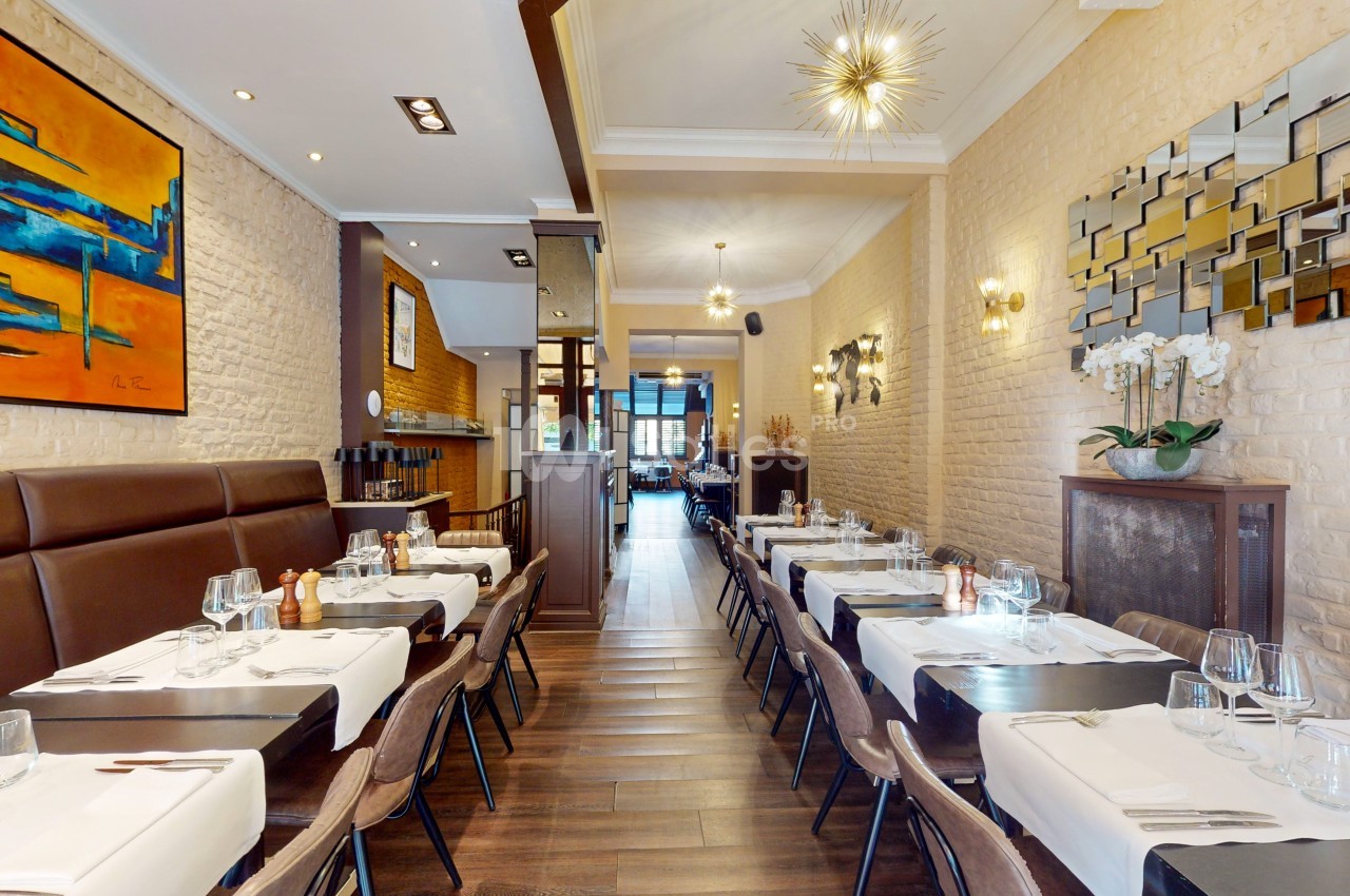 Salle de restaurant moderne avec tables dressées, murs en briques, décorations murales et éclairage chaleureux.