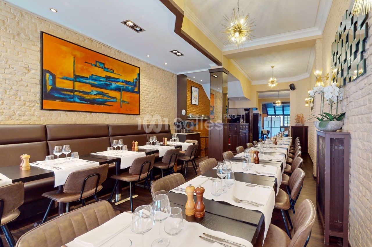 Salle de restaurant élégante avec tables dressées, murs en briques, tableau coloré et éclairage moderne.