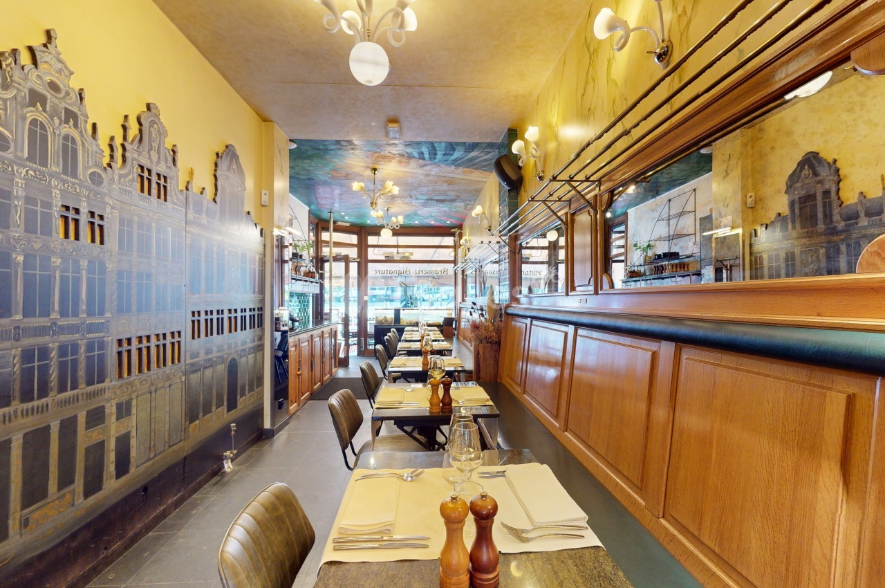 Salle de restaurant avec tables dressées, décor mural représentant des bâtiments et miroirs sur les murs.