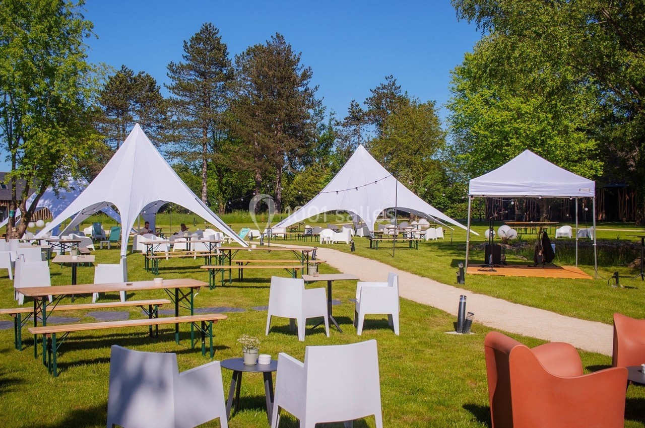 Chaises et tables disposées sur une pelouse avec des tentes blanches en arrière-plan sous un ciel dégagé.