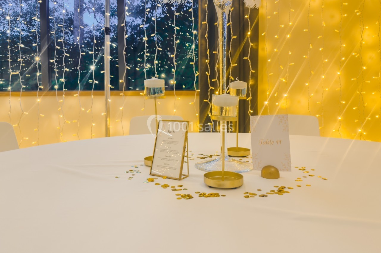 Table décorée avec des bougies, confettis dorés et un menu, devant une fenêtre ornée de guirlandes lumineuses.