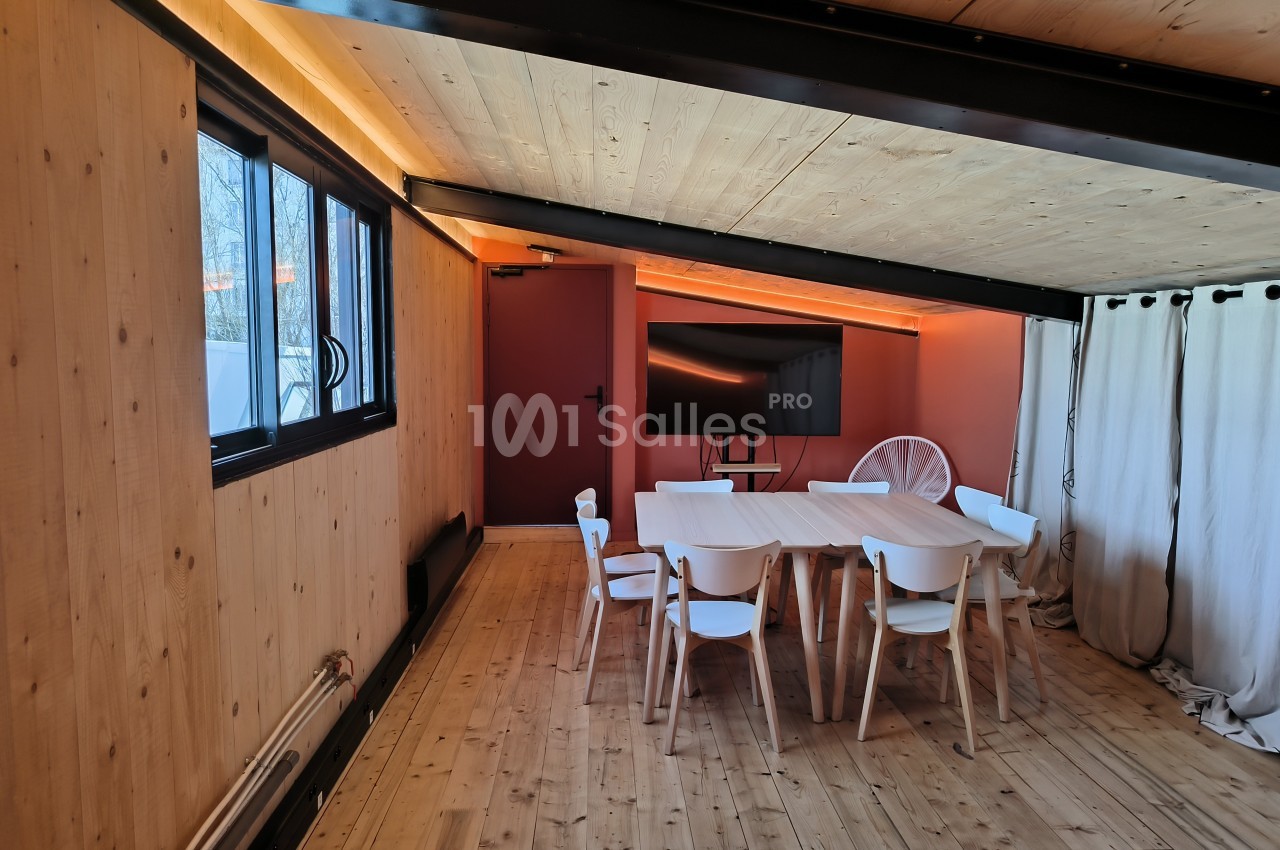 Salle de réunion avec table en bois, chaises blanches, écran mural et murs en bois et rouge.