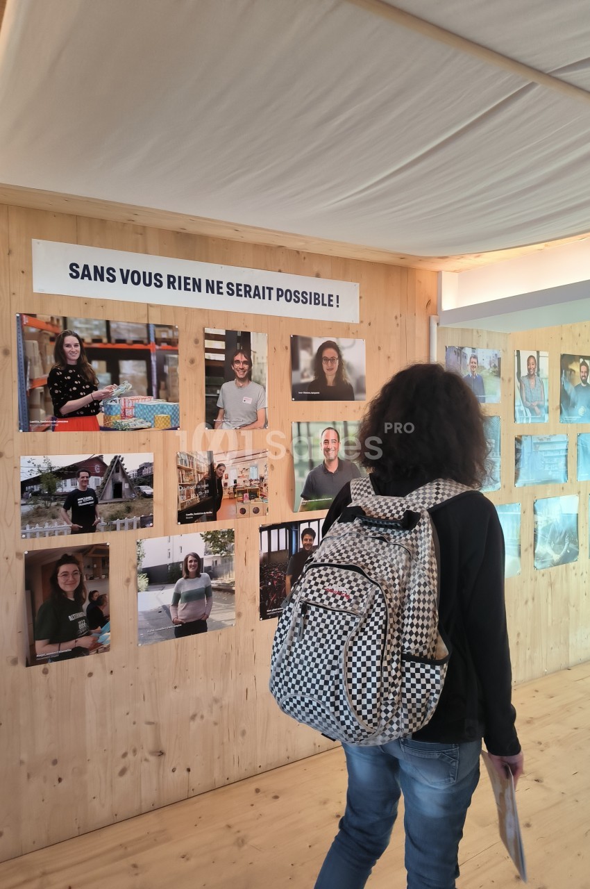 Une personne observe un mur d'exposition avec des portraits et un panneau indiquant ’Sans vous rien ne serait possible !’.