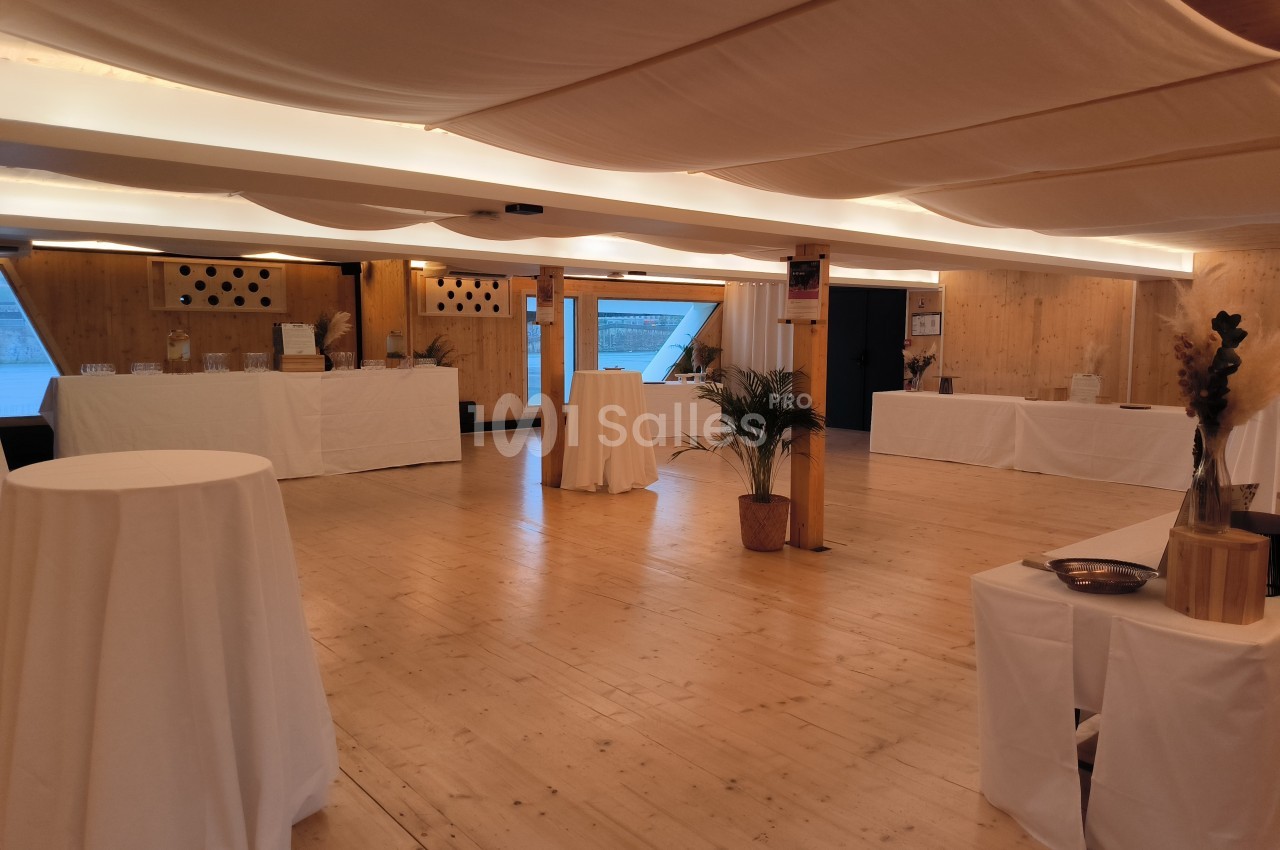 Salle lumineuse avec parquet en bois, tables hautes drapées de blanc et décorations minimalistes.