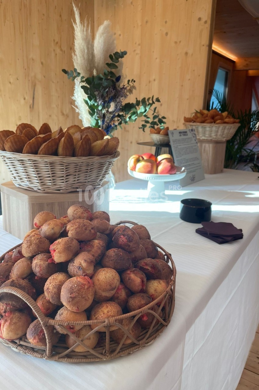 Table dressée avec des paniers de viennoiseries, pommes et décoration florale dans un espace en bois lumineux.