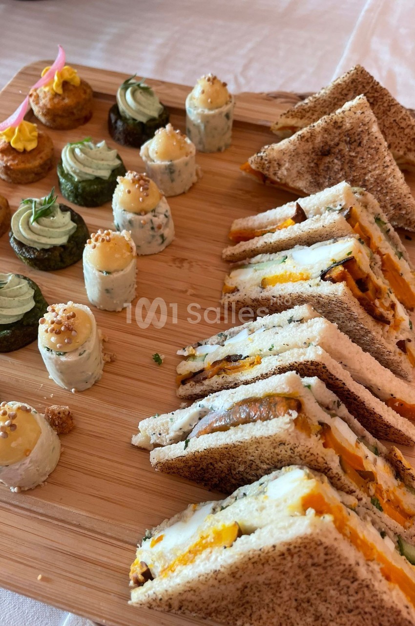 Plateau en bois avec des sandwichs triangulaires, des bouchées salées et des roulés garnis, disposés pour un apéritif.
