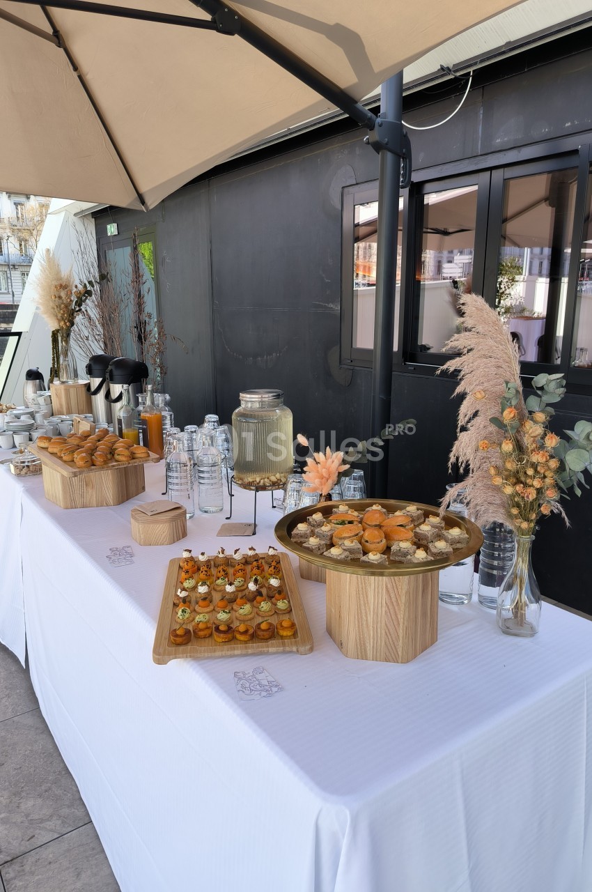 Buffet en extérieur avec boissons, verrines, pâtisseries et décorations florales sur une table blanche.
