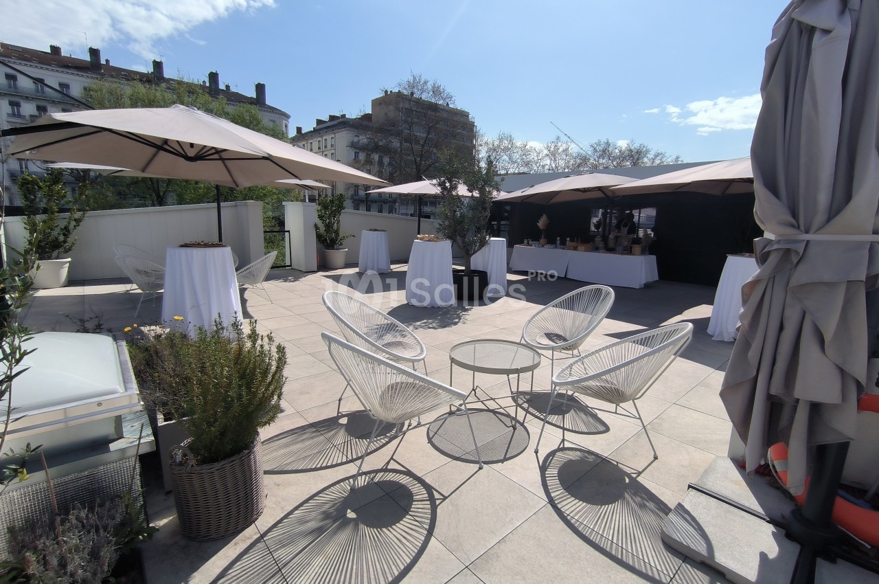 Terrasse aménagée avec des tables hautes, des chaises design, des parasols et des plantes sous un ciel ensoleillé.