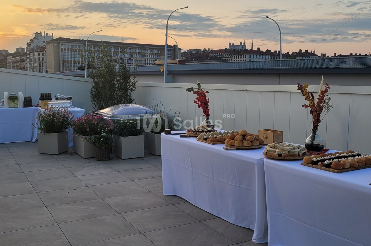 Buffet dressé sur une terrasse au coucher du soleil, avec vue sur des bâtiments urbains en arrière-plan.