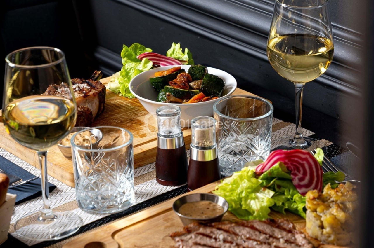 Repas composé de viande grillée, légumes sautés, salade, verres de vin blanc et condiments sur une table élégante.