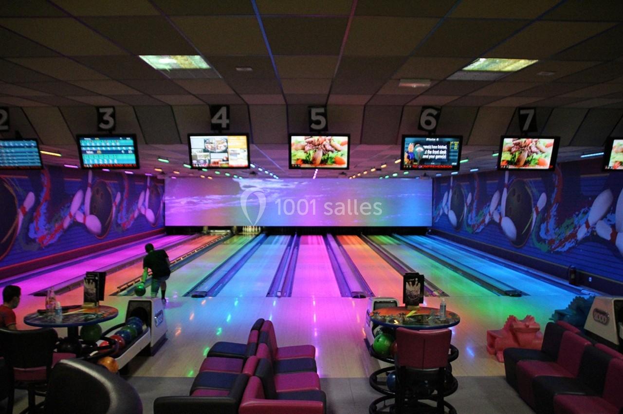 Salle de bowling avec plusieurs pistes éclairées par des lumières colorées et des écrans suspendus au plafond.