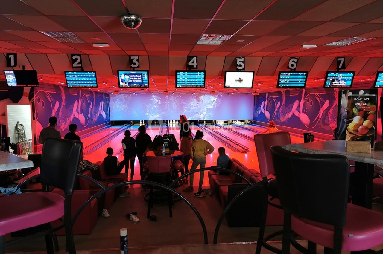 Des personnes jouent au bowling dans une salle colorée avec des écrans affichant les scores au-dessus des pistes.