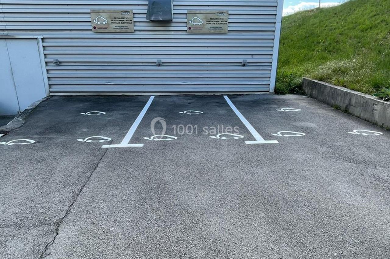 Places de stationnement réservées aux véhicules électriques, avec marquages au sol et panneaux sur un mur métallique.