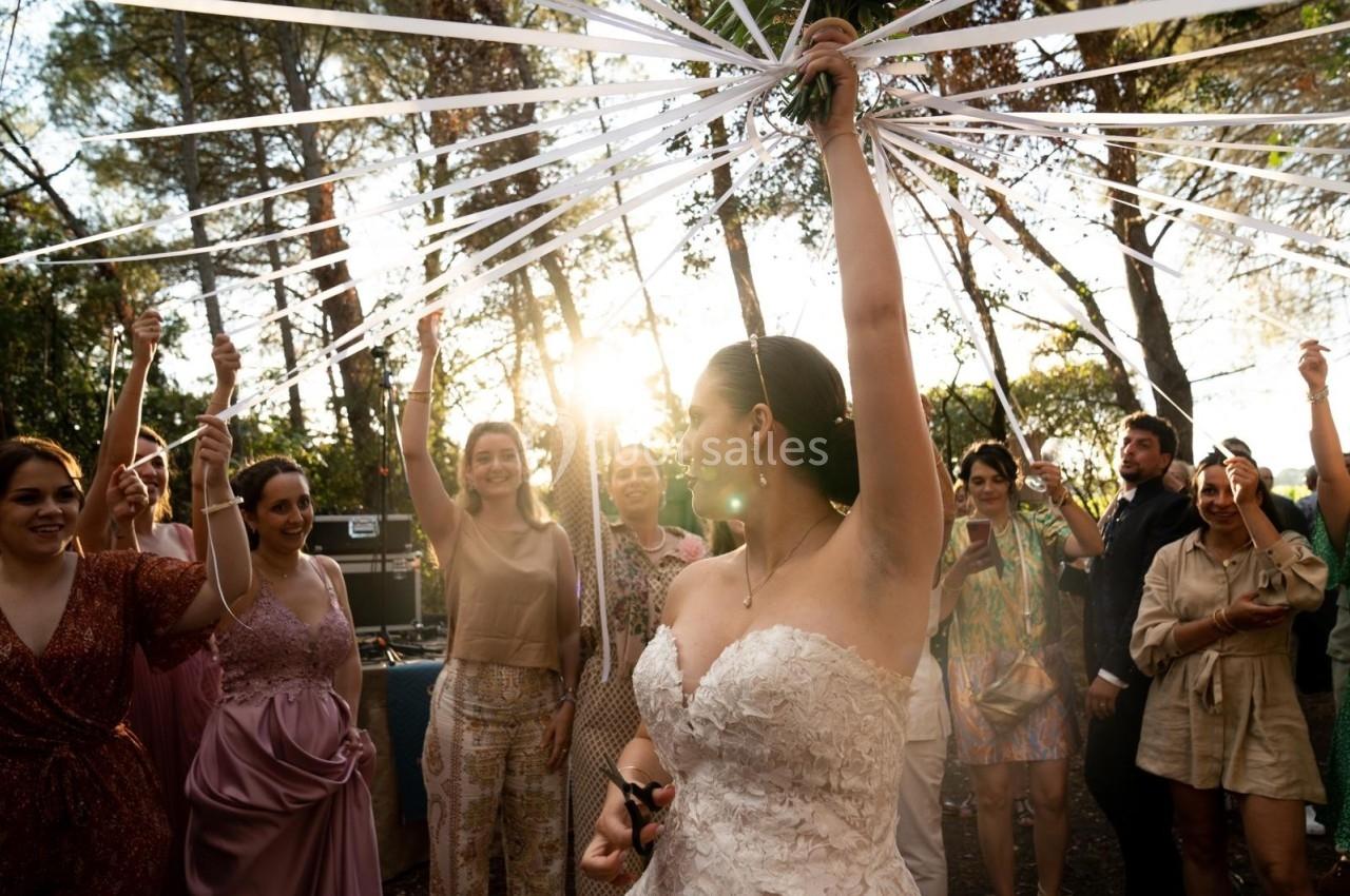 Une mariée entourée d'invités tient des rubans blancs sous un soleil couchant dans un cadre extérieur boisé.