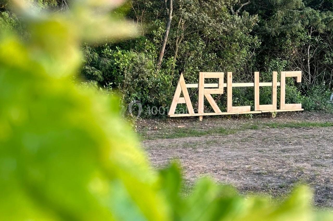 Panneau en bois formant le mot ’ARLUC’ installé dans un espace naturel entouré de végétation.