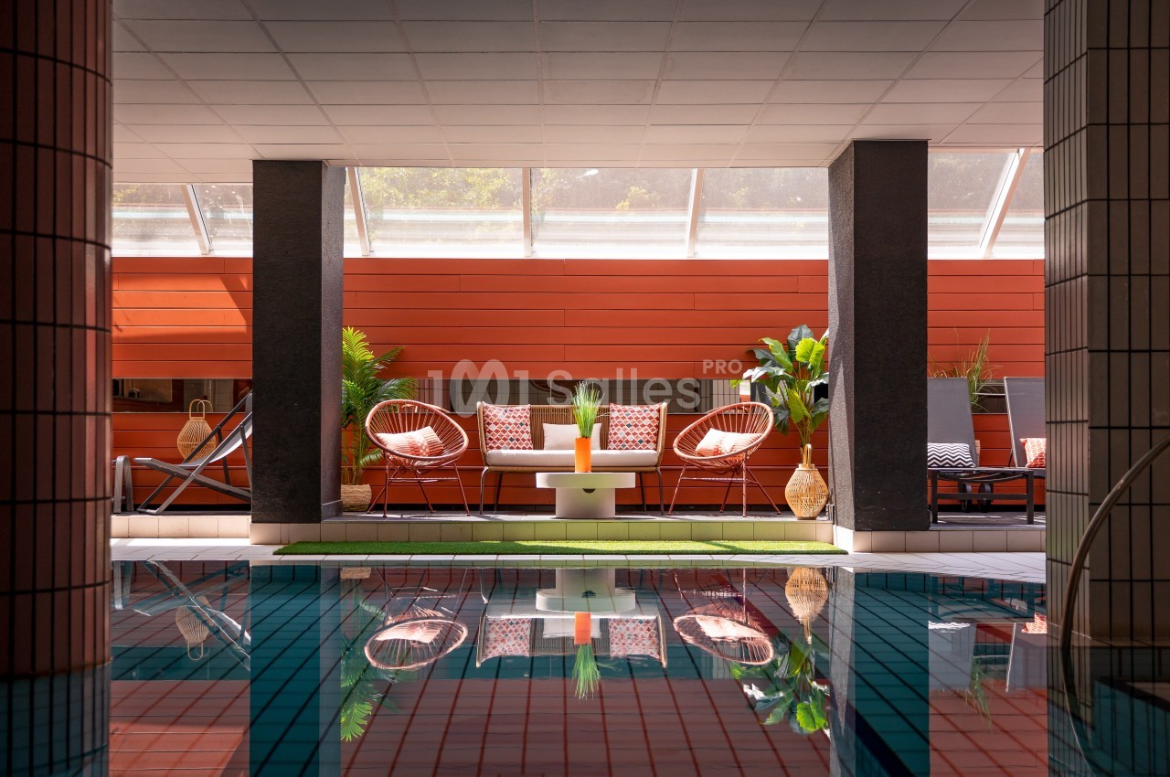 Espace détente avec fauteuils, coussins colorés, plantes et lumière naturelle, près d'une piscine intérieure.