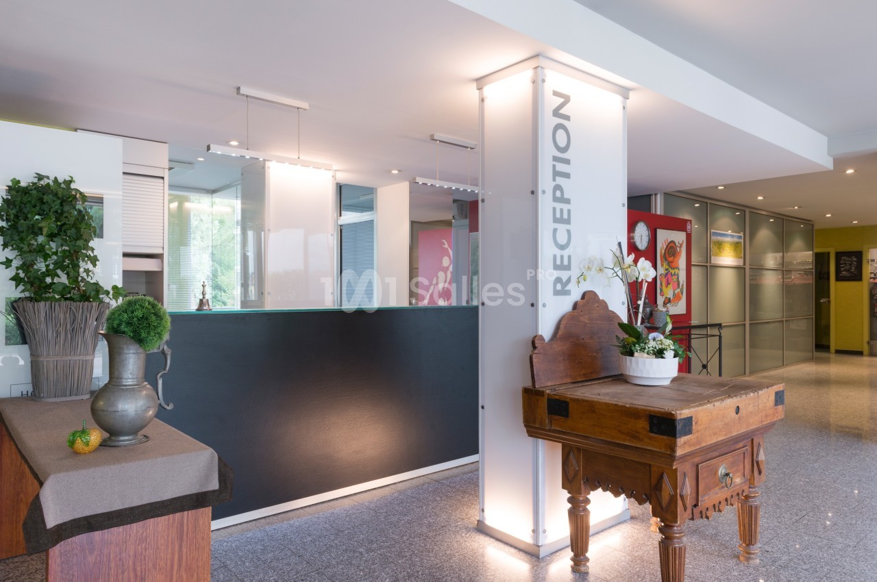 Accueil d'un espace intérieur moderne avec un comptoir de réception, une table en bois et des décorations végétales.