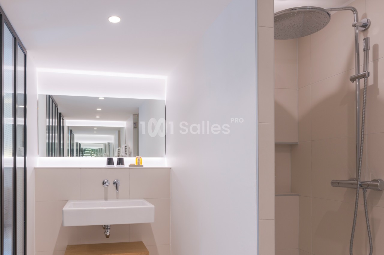 Salle de bain moderne avec lavabo suspendu, grand miroir lumineux et douche à effet pluie.