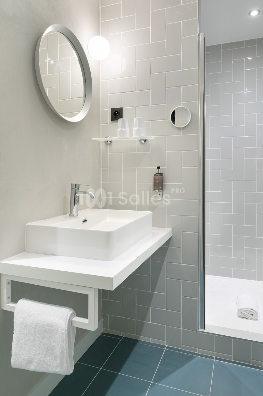 Salle de bain moderne avec lavabo blanc, miroir rond, porte-serviette et douche à paroi vitrée.