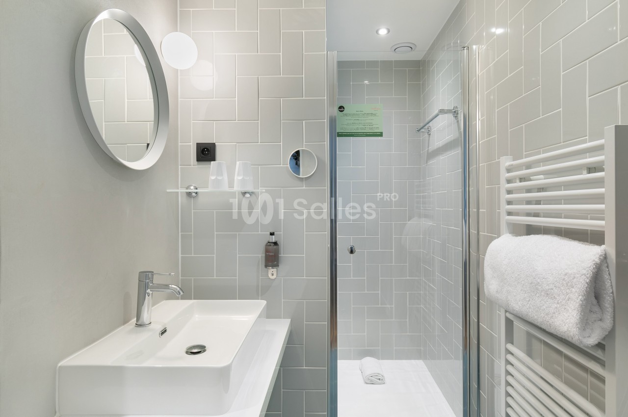 Salle de bain moderne avec lavabo, miroir rond, douche vitrée et porte-serviettes mural avec serviette blanche.