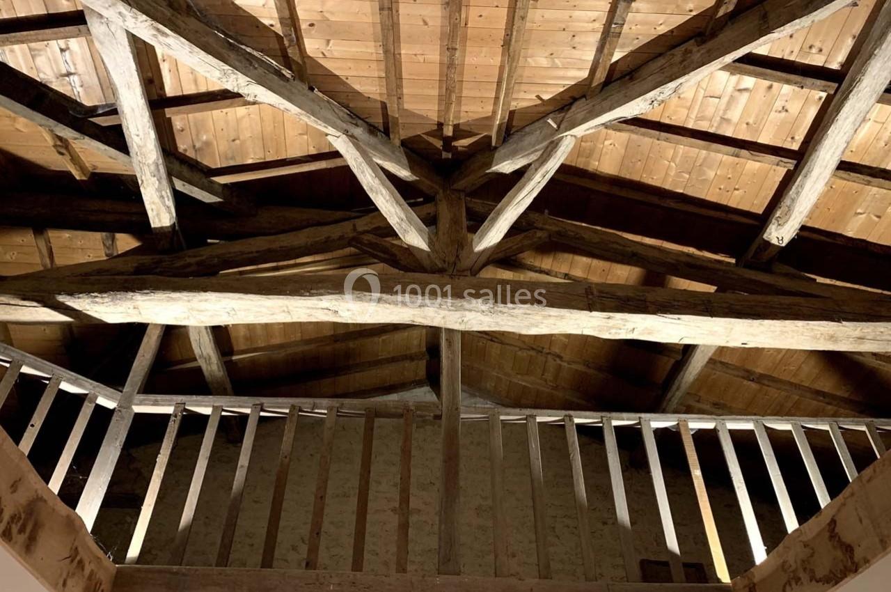 Charpente en bois apparente d'un plafond sous un toit, vue depuis une mezzanine avec garde-corps en bois.