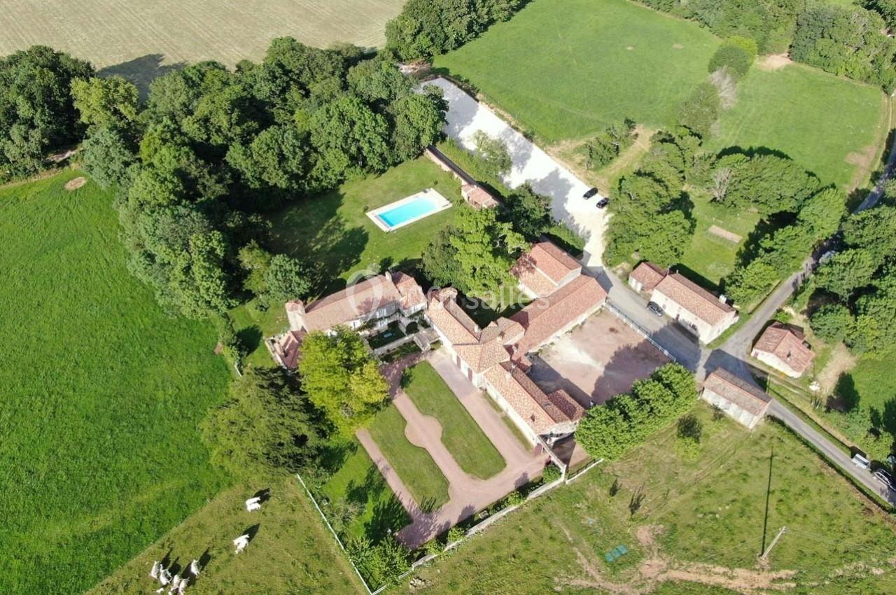 Vue aérienne d'un domaine rural avec bâtiments en pierre, piscine, espaces verts et pâturages environnants.