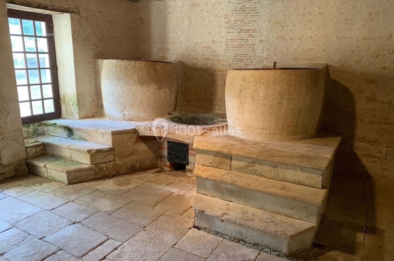 Deux cuves en pierre dans une pièce ancienne avec sol en dalles, murs en pierre et une fenêtre à gauche.