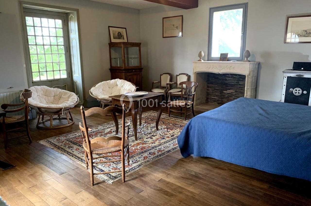 Chambre lumineuse avec parquet, lit couvert d’un drap bleu, cheminée en pierre et mobilier en bois ancien.