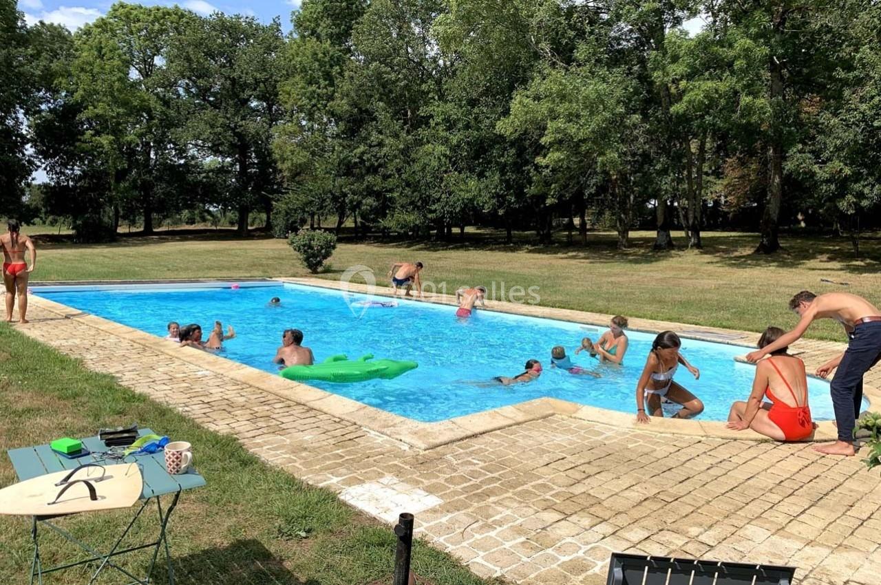Des personnes profitent d'une piscine extérieure entourée de pelouse et d'arbres par une journée ensoleillée.